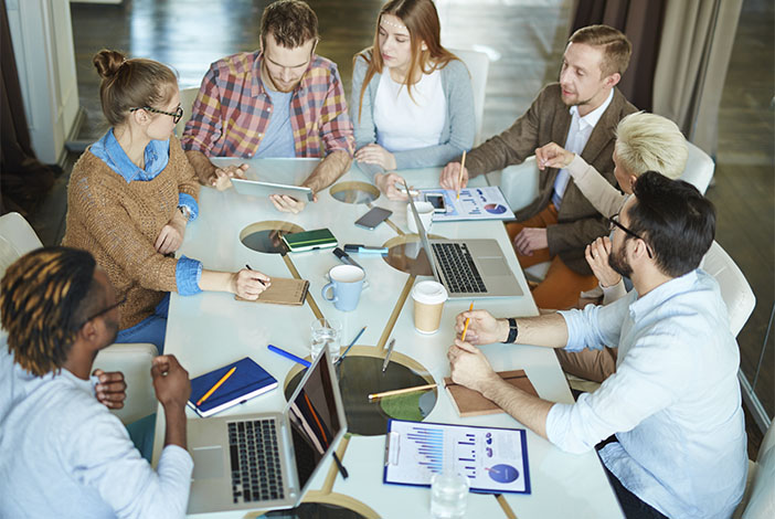 Equipo de oficina exponiendo ideas sobre una mesa de trabajo en la que hay varias laptops, cuadernos para notas y plumas y lápices.