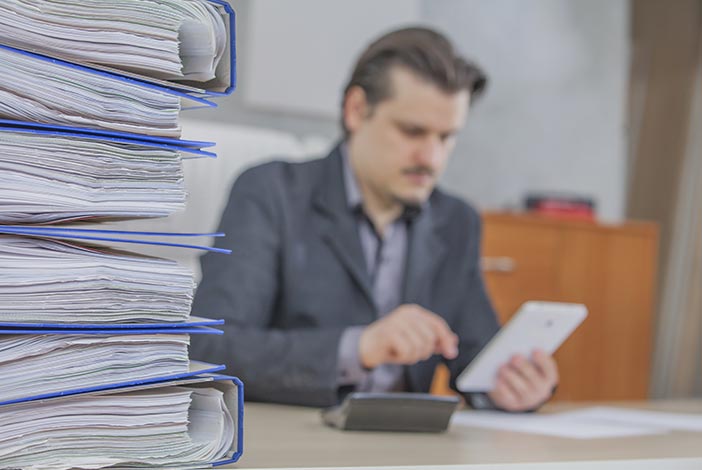 Empresario gestionando un gran número de documentos de manera tradicional.